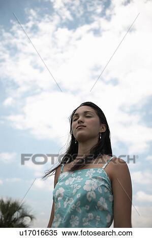 Young woman standing under blue sky, closing eyes View Large Photo Image Stock Photography - Young woman standing under blue sky, closing eyes. Fotosearch