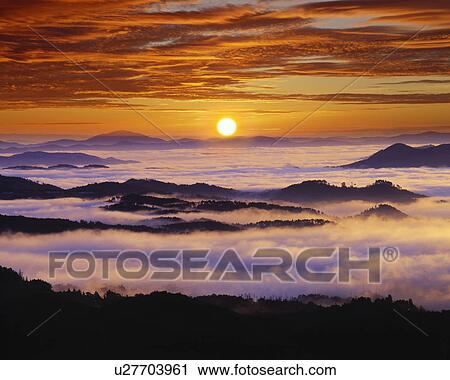 Stock Image - Fog shrouded mountain range at sunrise. Fotosearch
