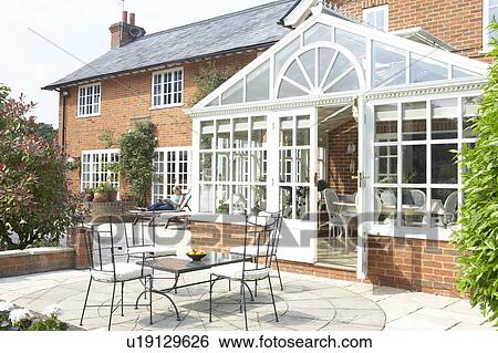 Stock Photograph - Exterior Of House With Conservatory And Patio. Fotosearch