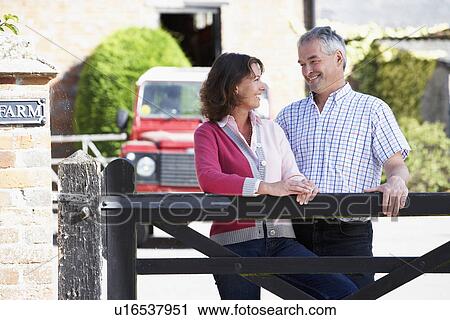 Stock Image - Farmer And Wife Looking Over Farm Gate. Fotosearch