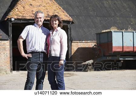 Stock Image - Farmer And Wife Standing In Front Of Farm Buildings. Fotosearch