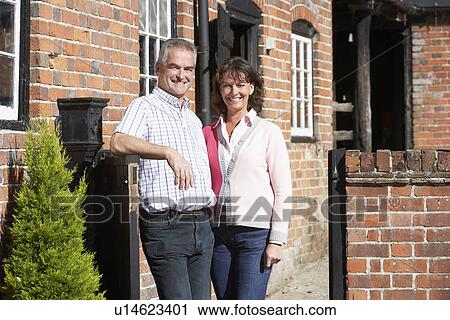 Stock Image - Farmer And Wife Standing In Front Of Farmhouse. Fotosearch