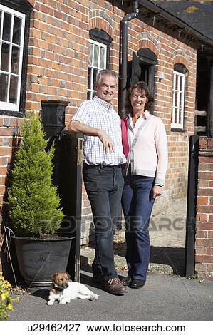 Stock Photo - Farmer And Wife Standing In Front Of Farmhouse. Fotosearch
