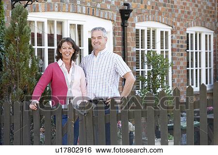 Stock Photograph - Farmer And Wife Standing In Front Of Farmhouse. Fotosearch