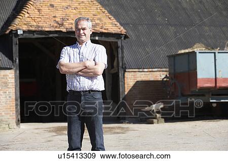 Stock Photo - Farmer Standing In Front Of Farm Buildings. Fotosearch