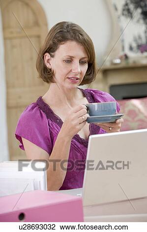 Stock Image - Woman drinking coffee at her desk. Fotosearch