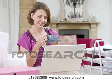 Woman drinking coffee at her desk View Large Photo Image Stock Photo - Woman drinking coffee at her desk. Fotosearch