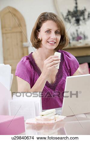 Picture - Woman eating lunch at her desk. Fotosearch