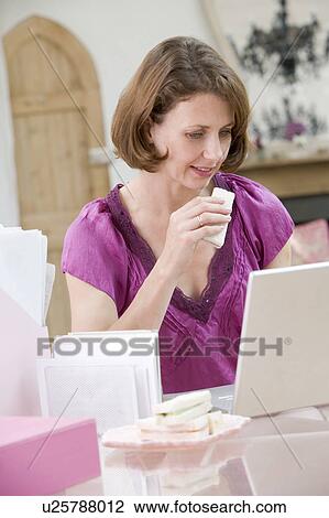 Stock Image - Woman eating lunch at her desk. Fotosearch