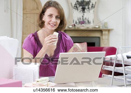 Stock Photograph - Woman eating lunch at her desk. Fotosearch