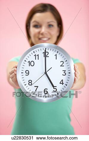 Stock Image - Woman Holding Clock Showing 5 O'Clock. Fotosearch