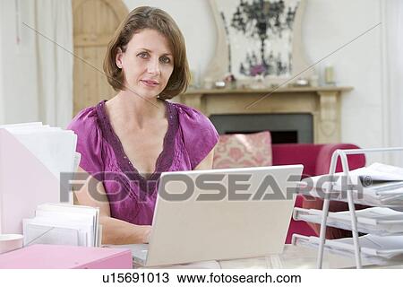 Stock Image - Woman sitting at desk and using laptop. Fotosearch