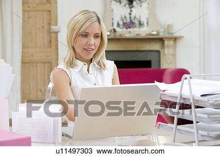 Stock Image - Woman sitting at her desk using laptop. Fotosearch