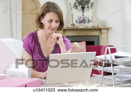 Stock Image - Woman sitting at her desk using laptop. Fotosearch
