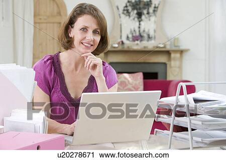 Stock Image - Woman sitting at her desk using laptop. Fotosearch