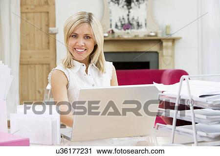 Stock Image - Woman sitting at her desk using laptop. Fotosearch