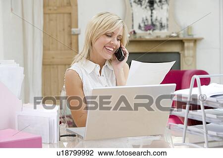 Stock Image - Woman using laptop and talking on phone. Fotosearch