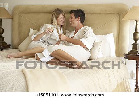 Stock Image - Young Couple Enjoying Champagne In Bedroom. Fotosearch