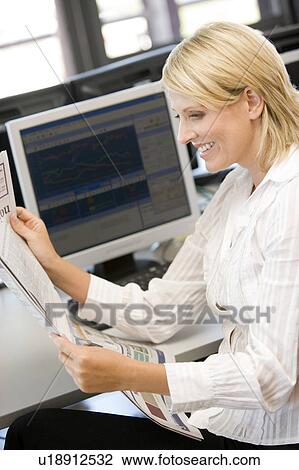 Stock Image - Businesswoman Reading Newspaper At Work Desk. Fotosearch