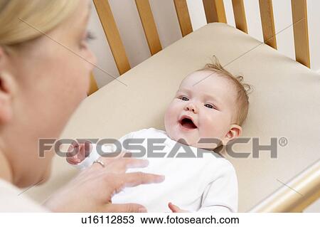 Stock Image - Mother Playing With Baby In Cot. Fotosearch