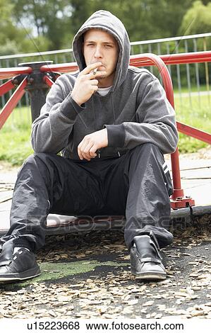 Stock Photo - Young Man Sitting In Playground Smoking Joint. Fotosearch