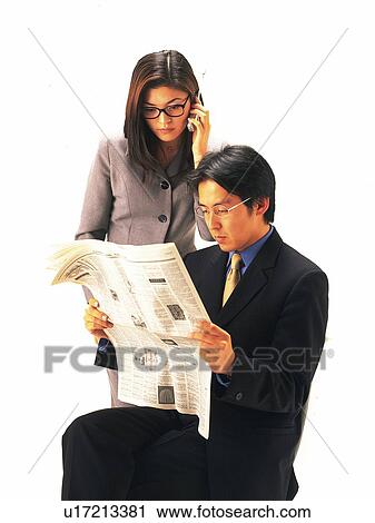 Stock Image - Businessman and businesswoman reading news paper together, Front View. Fotosearch