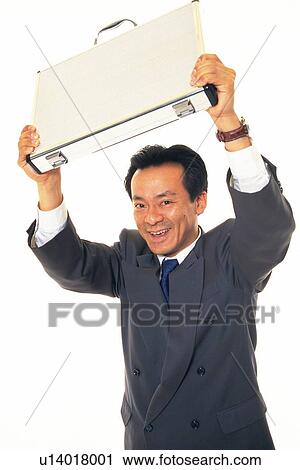 Stock Image - Businessman holding business case up in the air with smile, Front View. Fotosearch