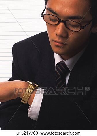 Stock Photo - Businessman looking at watch, Front View. Fotosearch