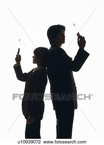 Stock Image - Bsinessman and businesswoman standing back to back and using mobile phone, Side View, Silhouette . Fotosearch