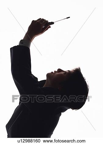 Stock Image - Bsinessman looking up at raised mobile phone, Side View, Silhouette . Fotosearch