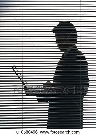 Stock Photograph - Bsinessman standing and using laptop computer by the blind, Side View, Silhouette . Fotosearch