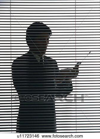 Stock Photograph - Bsinessman standing and using mobile phone by the blind, Side View, Silhouette . Fotosearch