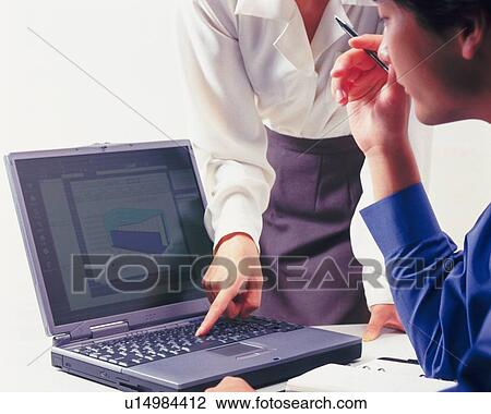 Stock Image - Businessman and businesswoman working with a computer at the desk, Portrait, Side View, High Key. Fotosearch