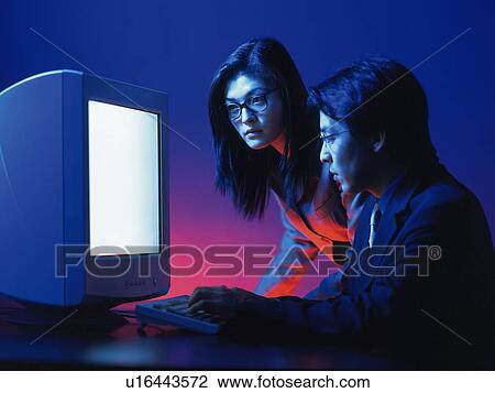 Stock Image - Businessman and businesswoman working with a computer at the desk, Portrait, Side View, Toned Image. Fotosearch