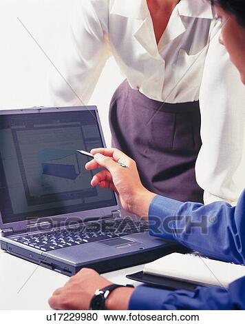 Stock Image - Businessman and businesswoman working with a computer at the desk, Portrait, Side View. Fotosearch