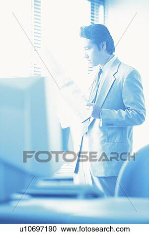 Stock Image - Businessman reading news paper by the Window, Portrait, Side View, Toned Image. Fotosearch
