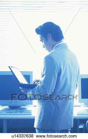 Businessman standing and working with a laptop computer by the desk, Portrait, Rear View, High Key, Toned Image View Large Photo Image Stock Photo - Businessman standing and working with a laptop computer by the desk, Portrait, Rear View, High Key, Toned Image. Fotosearch