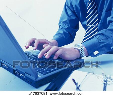 Stock Image - Hands working with a computer at the desk, Side View, Toned Image. Fotosearch