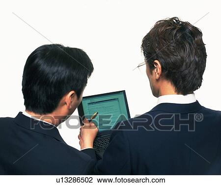 Stock Image - Two businessmen working with a computer at the desk, Portrait, Rear View, High Angle View. Fotosearch