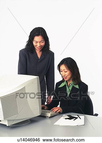 Stock Photograph - Two businesswomen working with a computer at the desk, Portrait, Front View. Fotosearch