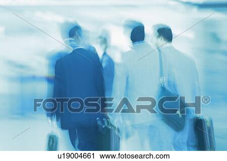 Stock Image - Business people walking and holding bags, rear view, blurred motion, Tokyo, Japan. Fotosearch