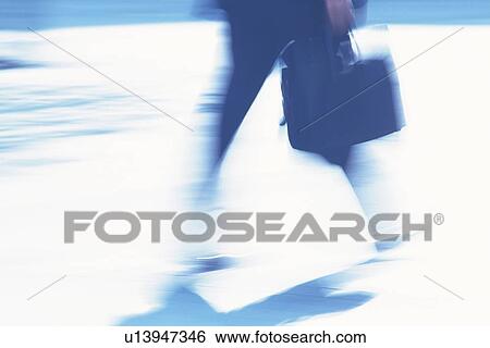Stock Photograph - Businessman walking and holding briefcase, side view, blurred motion, Tokyo, Japan. Fotosearch