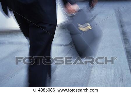 Stock Photograph - Businessman walking and holding briefcase, rear view, blurred motion, Tokyo, Japan. Fotosearch
