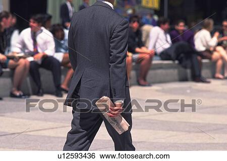 Stock Photograph - Businessman walking and holding a newspaper, rear view, New York City, NY, USA. Fotosearch