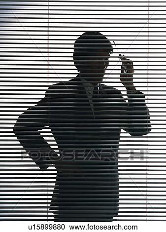 Stock Image - Businessman behind blind, using a mobile phone, front view. Fotosearch