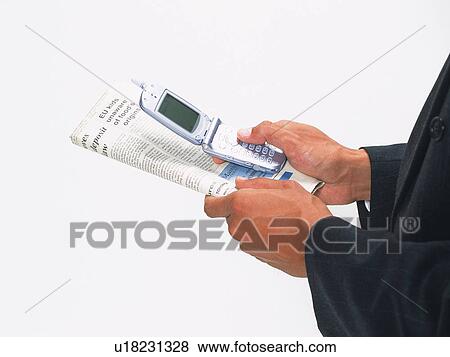 Stock Photo - Businessman holding a mobile phone and newspaper, high angle view. Fotosearch