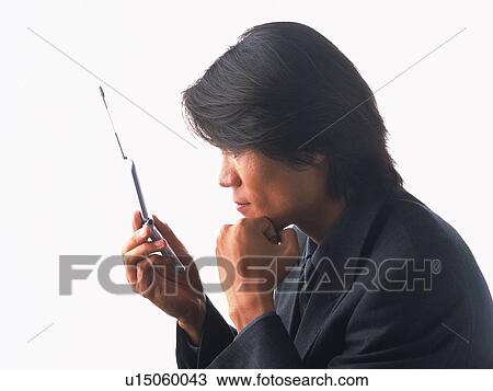 Stock Image - Businessman holding and looking at a mobile phone, resting chin on his fist, side view. Fotosearch