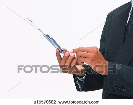 Stock Image - Businessman pushing buttons of mobile phone, side view. Fotosearch
