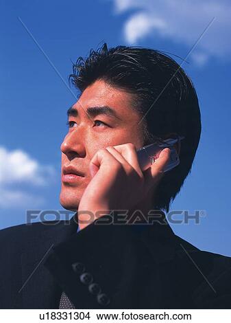 Picture - Businessman using a mobile phone under the blue sky, low angle view. Fotosearch