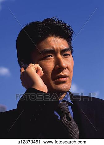 Stock Image - Businessman using a mobile phone under the blue sky, front view, close up. Fotosearch